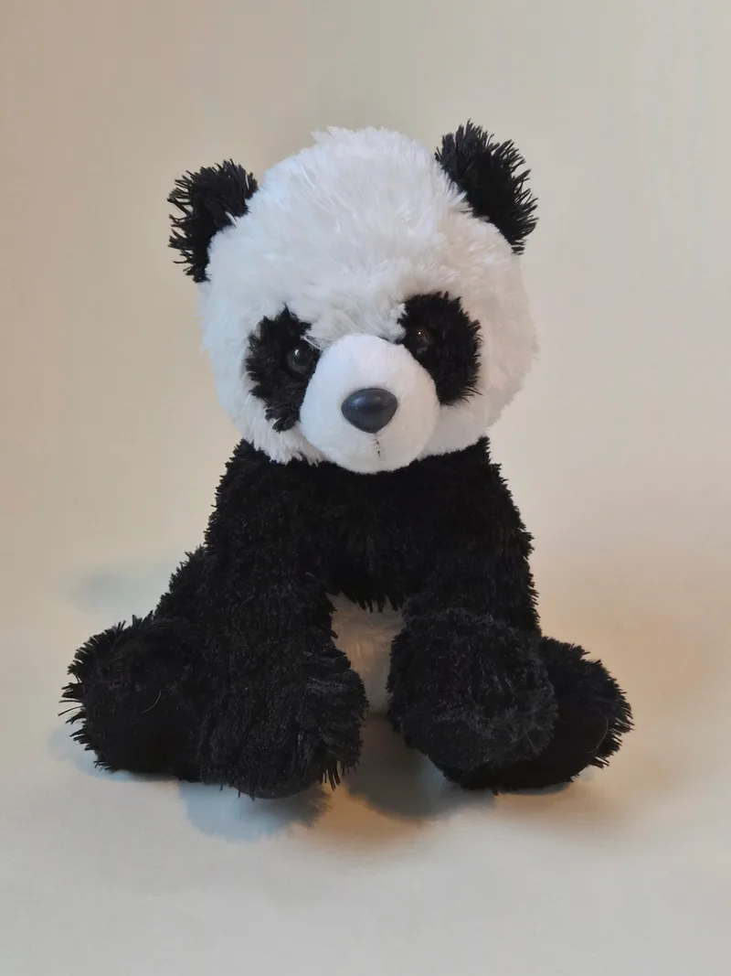 Plush black-and-white panda bear sitting upright against a plain cream background, with fluffy fur, dark eyes, and a gray stitched nose.