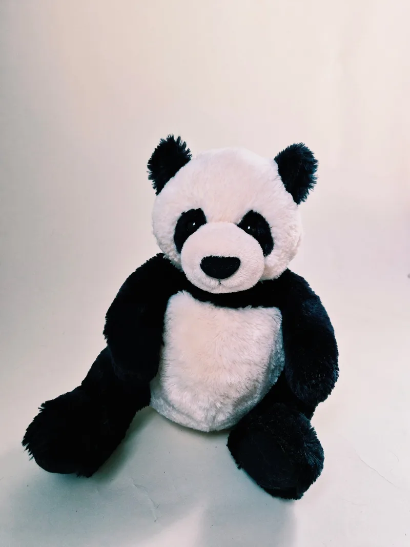 Black and cream GUND panda plush sitting upright against a plain pale background