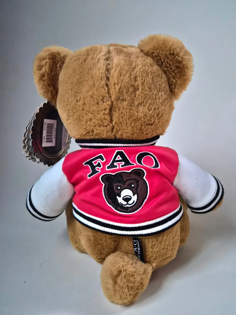Back view of the teddy bear showing FAO lettering and a bear crest on the red varsity jacket, with original hang tags visible near one ear