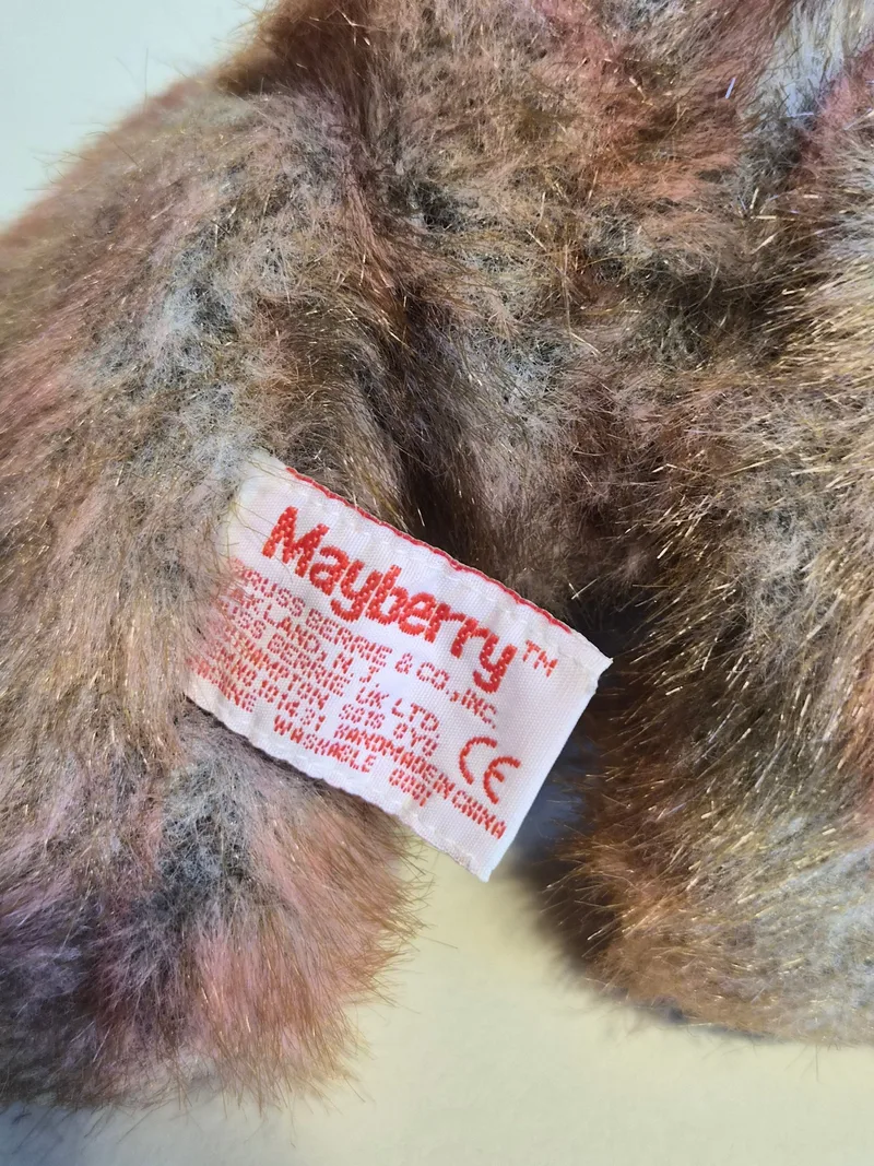 Close-up of the bear's white Mayberry fabric tag from Russ Berrie & Co., nestled in multi-toned fur with fine gold tinsel threads
