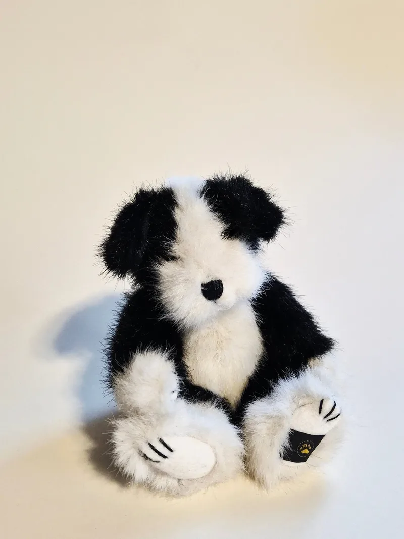 Small black and white plush skunk sitting upright, with fluffy fur, a black stitched nose, and embroidered claws on white felt paw pads