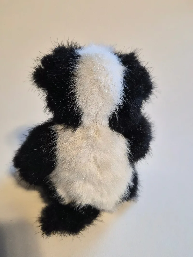 Back view of the plush skunk showing a wide white stripe running down black fur from head to tail
