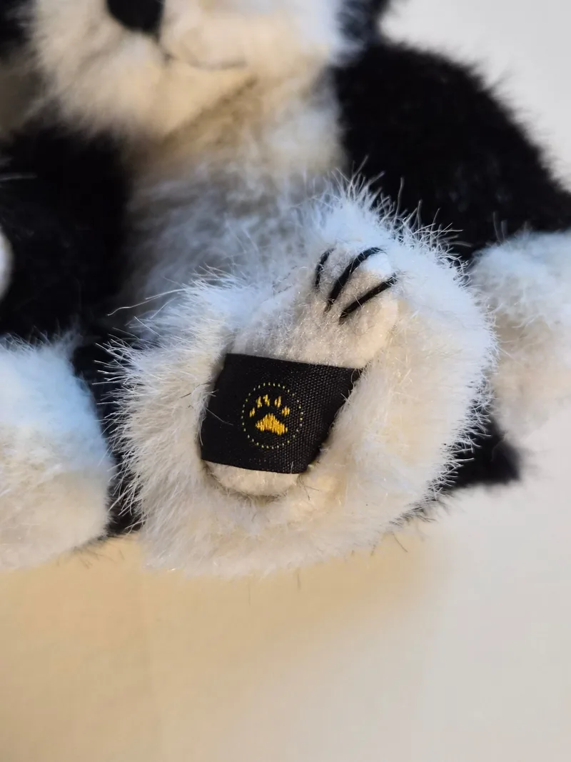 Close-up of the skunk's white felt foot pad with embroidered claw stitches and a black Boyds tag with a gold paw print
