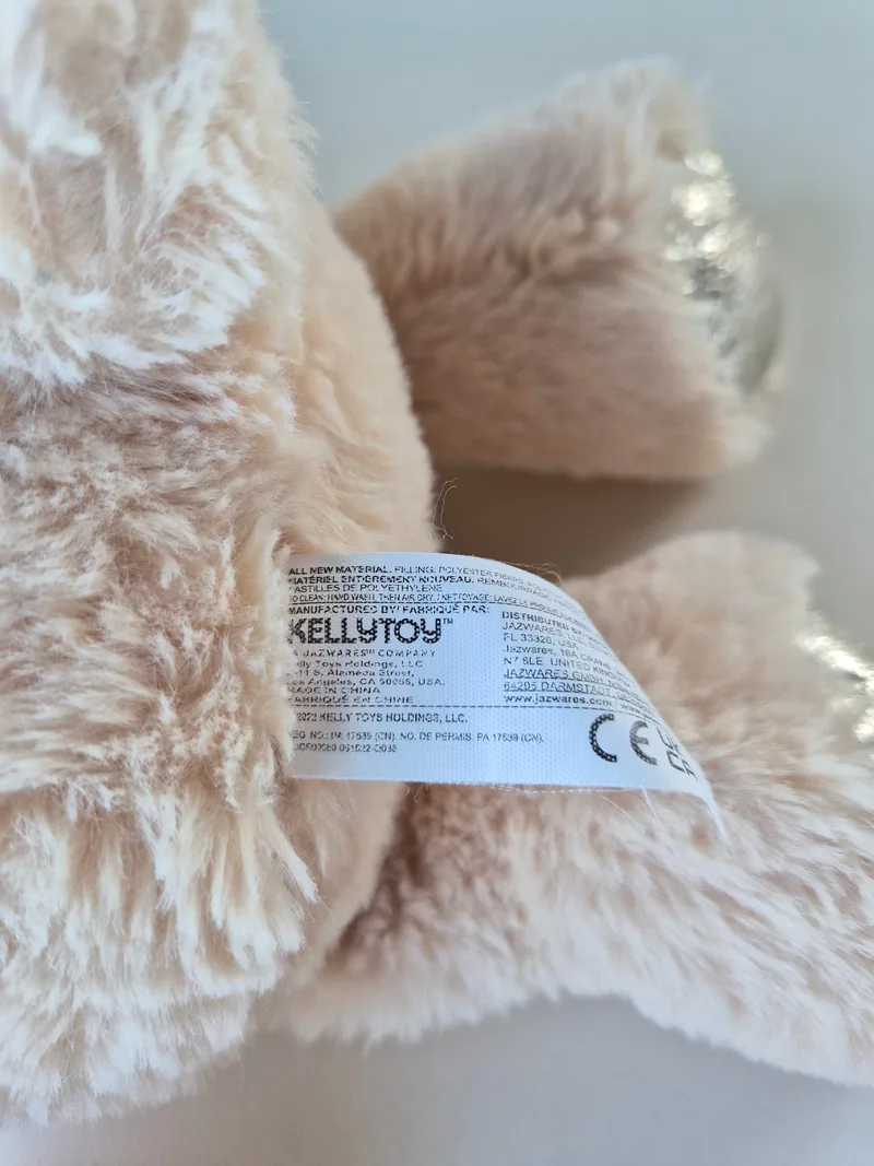 Sewn-in Kellytoy fabric tag on the bear's seam amid pale plush fur