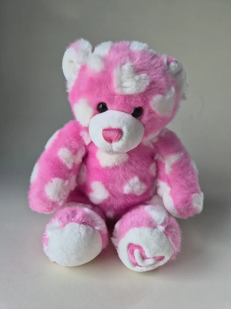 Seated pink-and-cream Build-A-Bear teddy with scattered white hearts, cream muzzle, and pink stitched nose