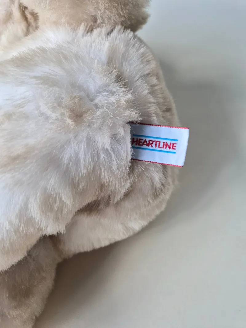 Close-up of the bear's ear and a white side-seam tag reading HEARTLINE in red and blue