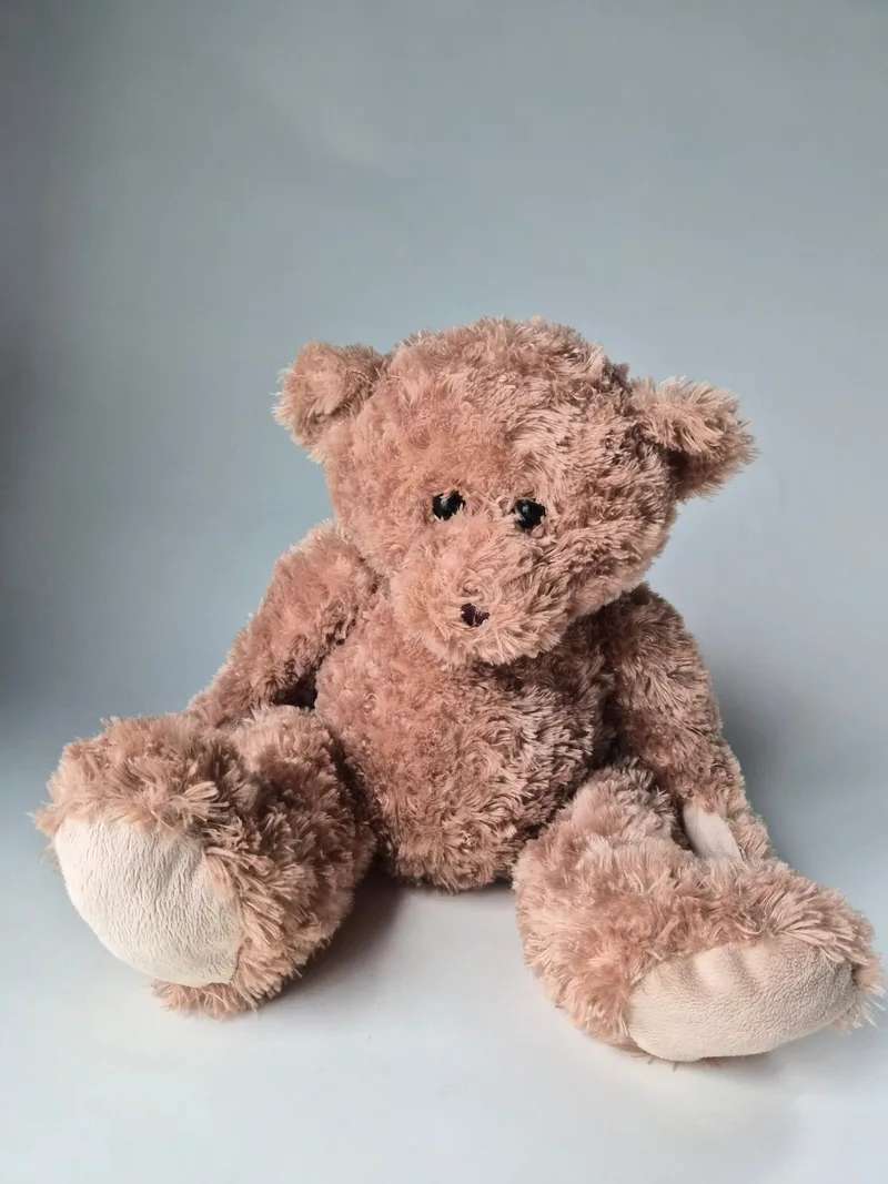 Caramel-brown shaggy teddy bear sitting with floppy limbs, ivory suede muzzle and foot pads, and small bead eyes