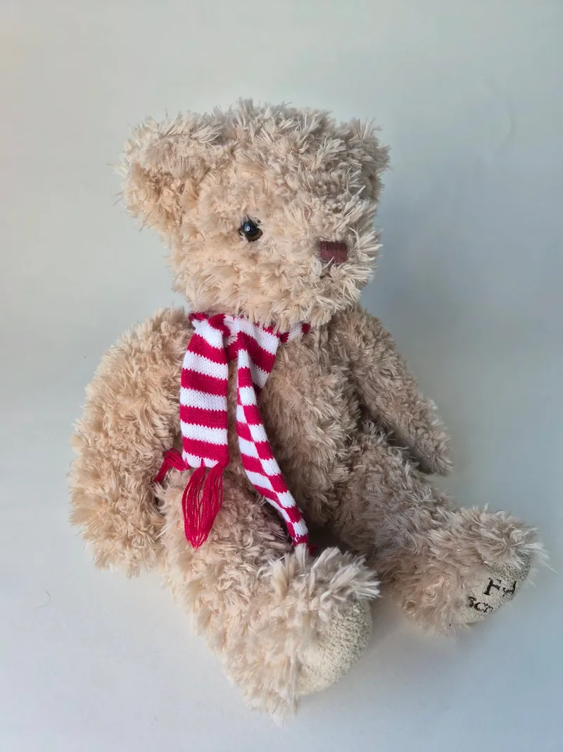 Champagne-blond curly FAO Schwarz teddy bear seated wearing a red and white striped knit scarf