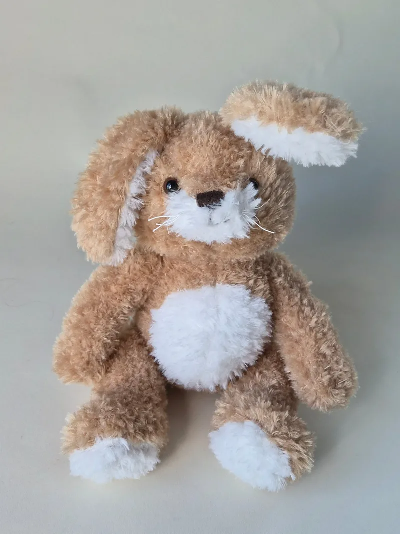 Almond-tan curly-plush bunny with long floppy ears, cream muzzle and belly, and long stitched whiskers, seated