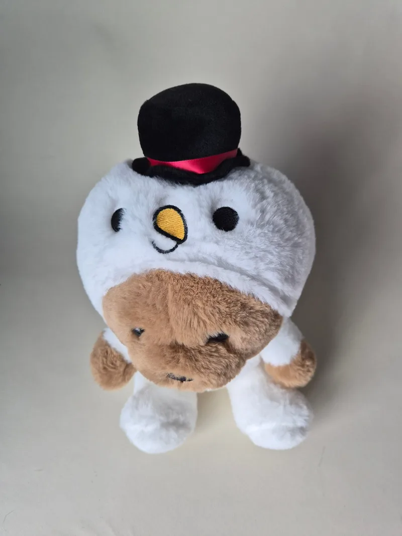 Top view of the bear's snowman hood showing a black eye, yellow felt carrot nose, and red-ribboned top hat above the brown muzzle