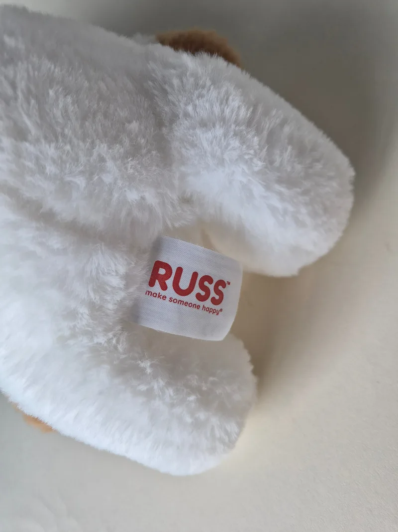 Close-up of a white fabric tag reading RUSS make someone happy stitched into the white plush costume