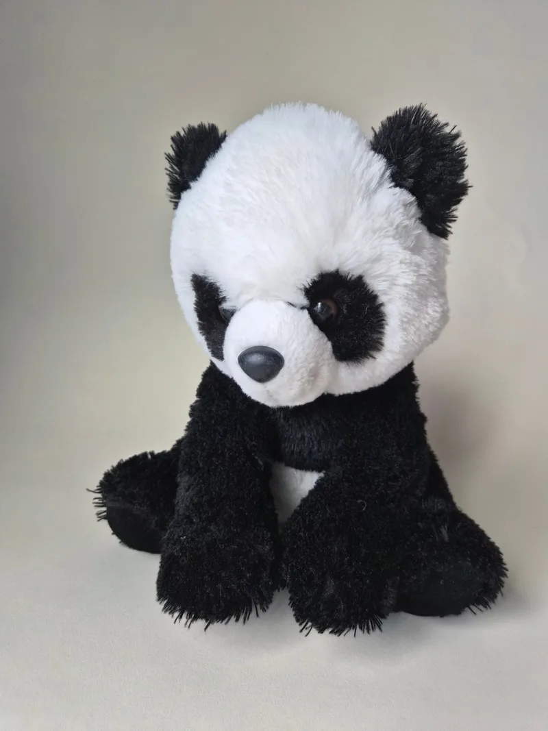 Front view of a black-and-white Aurora panda plush sitting upright with tilted eye patches and a charcoal nose