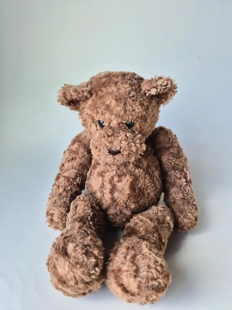Front view of a large curly cocoa-brown teddy bear sitting with floppy limbs and small black bead eyes