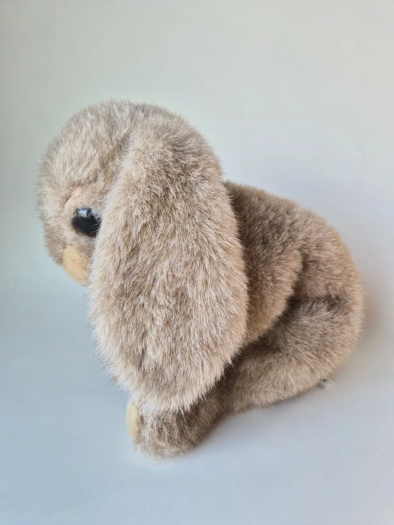 Frosted taupe lop-eared plush rabbit seen from the side with long ears drooping and dark bead eye