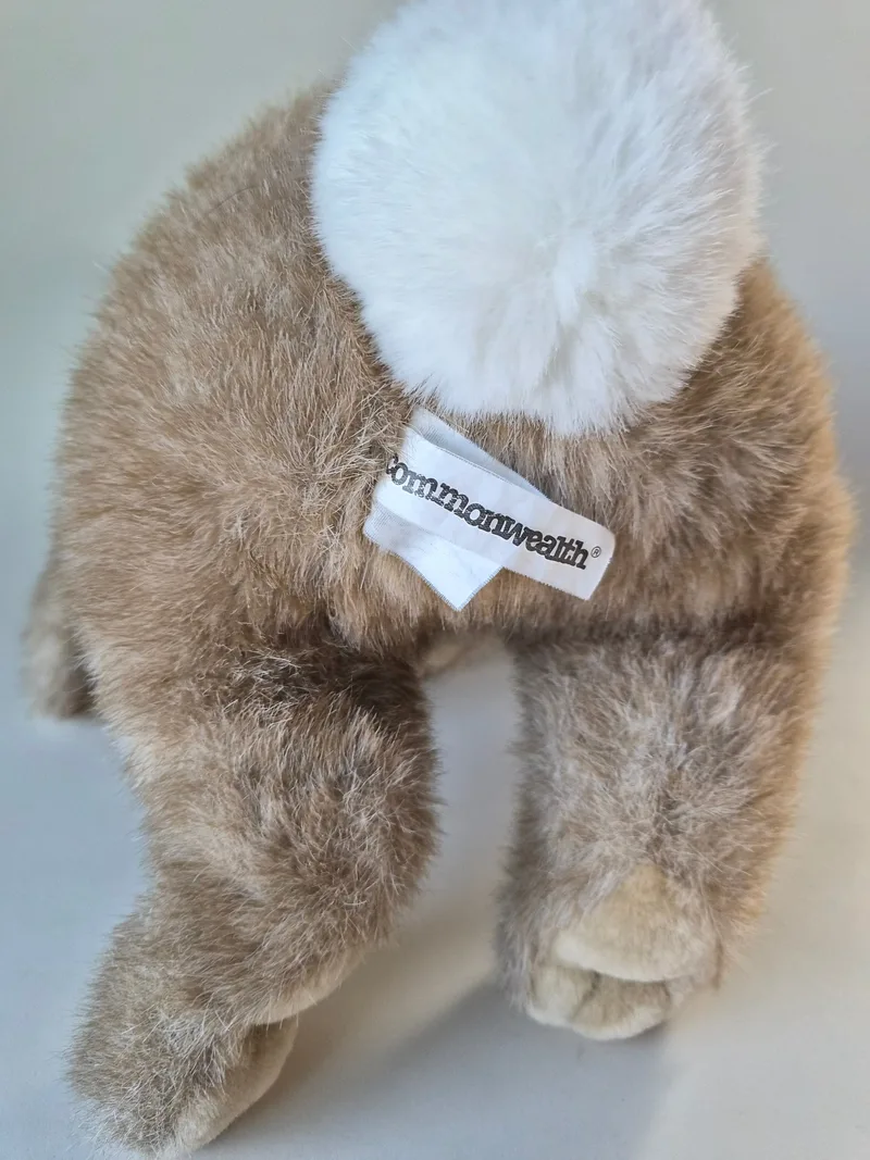 Back view of the rabbit showing a white pom tail and a woven Commonwealth label at the seam