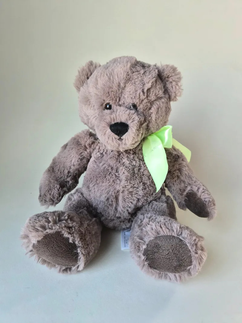 Grey swirl-shag teddy bear seated, wearing a spring-green satin bow, with darker felt muzzle and paw soles