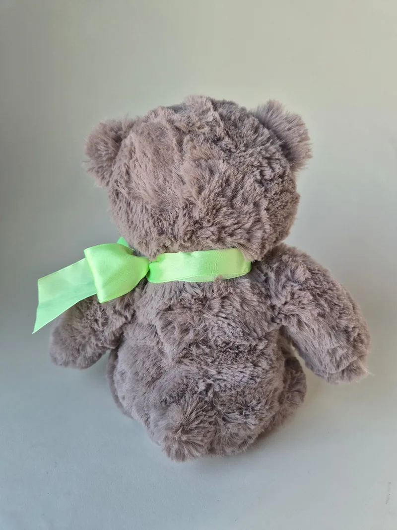 Back view of the grey teddy bear showing rounded body, swirled fur, and the tied green satin bow