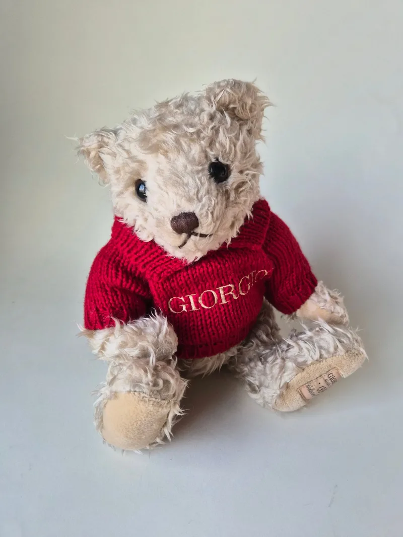 Cream mohair teddy bear seated, wearing a red knit sweater lettered GIORGIO in gold, with suede paw pads