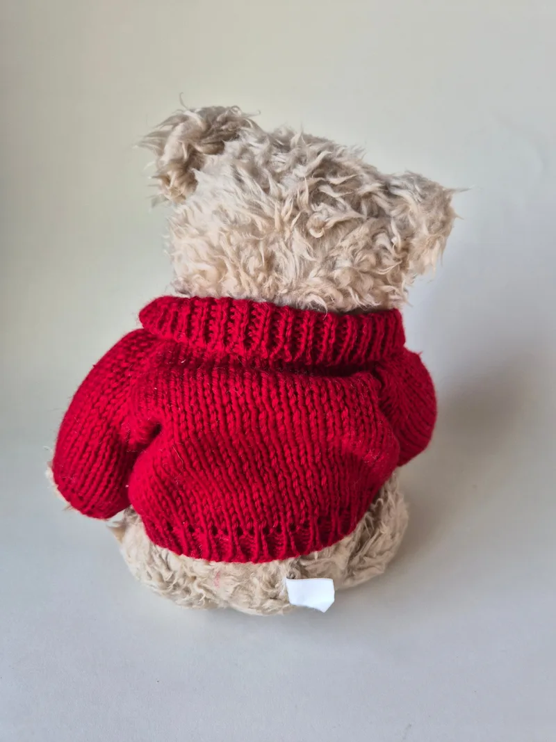 Back view of the bear showing the red knit sweater and aged oat-colored shaggy fur
