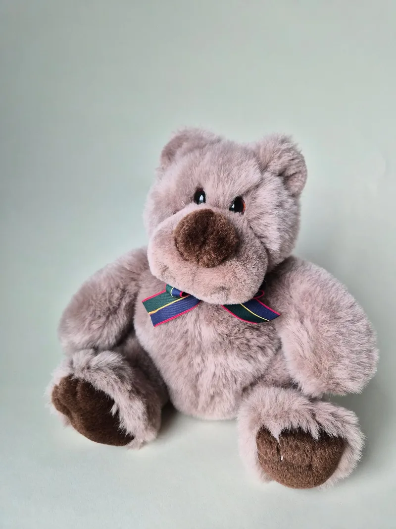 Front view of a plump taupe teddy bear with a dark cocoa muzzle and a navy, green, and crimson tartan ribbon at the neck