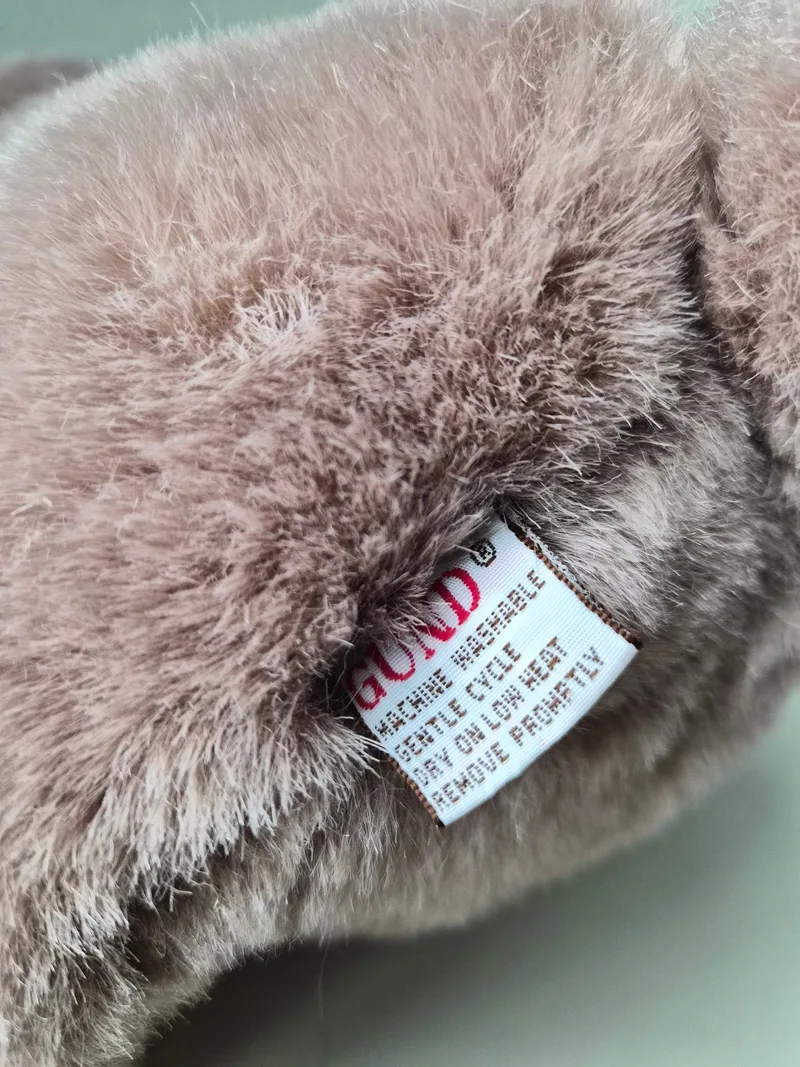 Close-up of the bear's white Gund care label with red washing-instruction text tucked into the seam