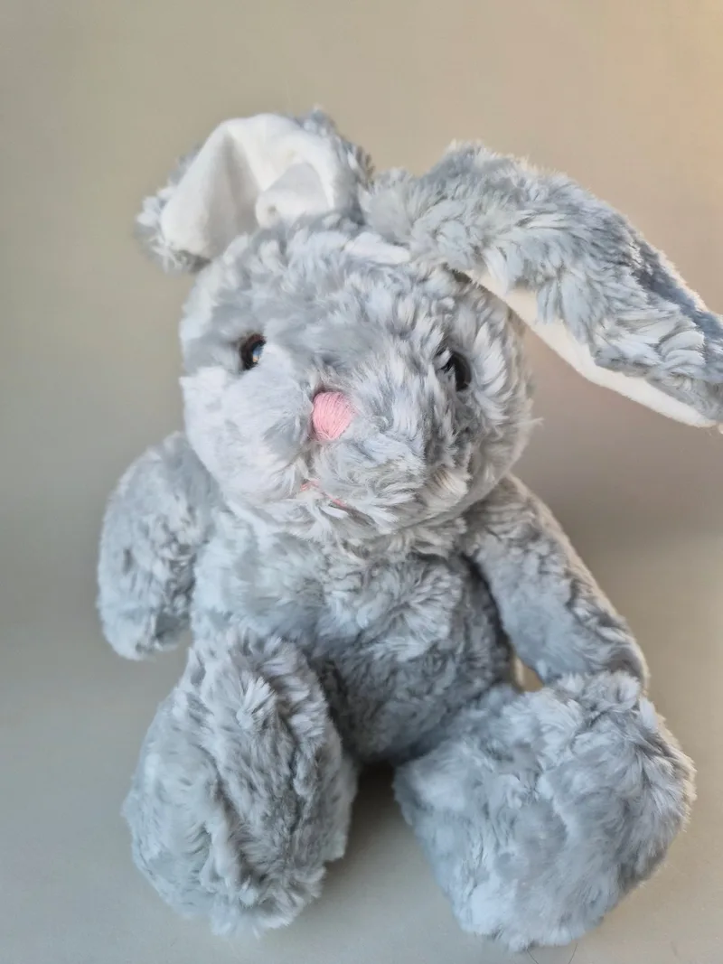 Grey plush bunny with wired ears bent to one side, pink stitched nose, seated