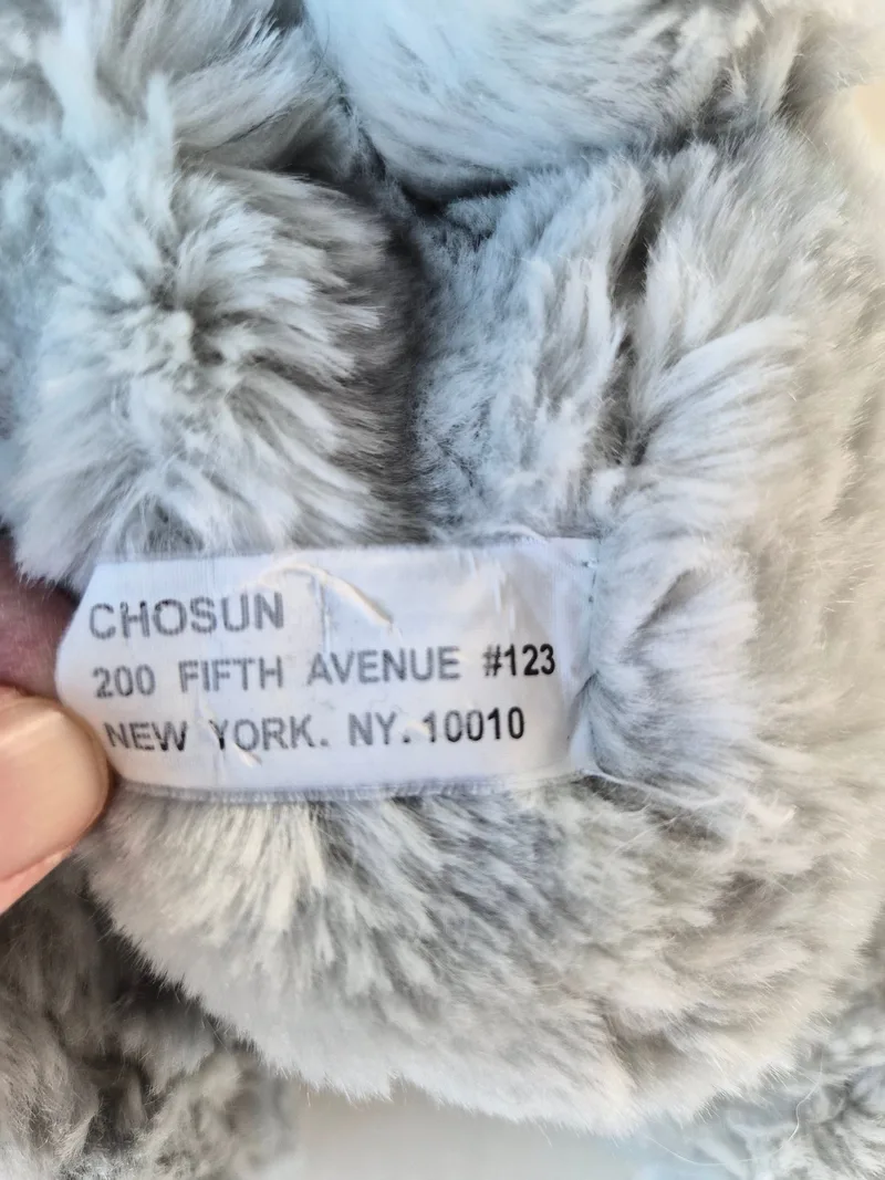 Close-up of a white Chosun sewn-in tag reading 200 Fifth Avenue, New York, NY 10010 on grey fur