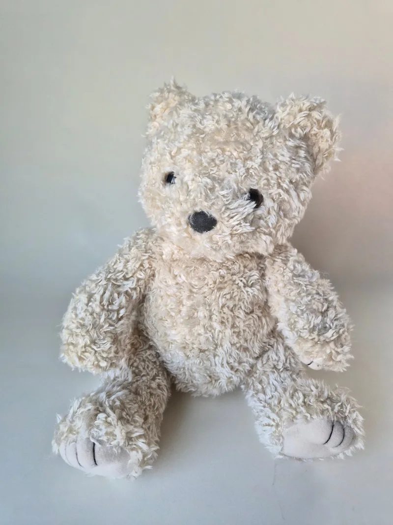 Seated ivory-and-wheat curly teddy bear with cream paw pads showing stitched claws