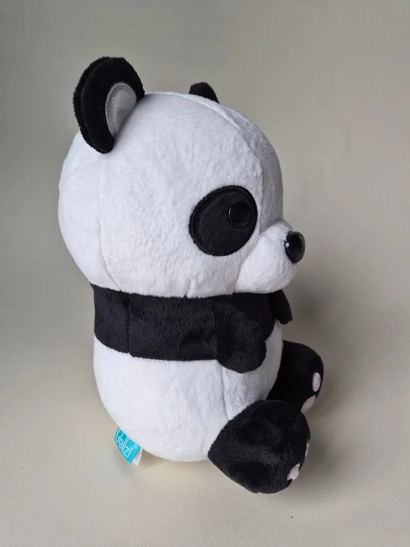 Side view of the panda plush showing grey-lined ear, black chest band and a teal Bellzi fabric tag at the hip seam