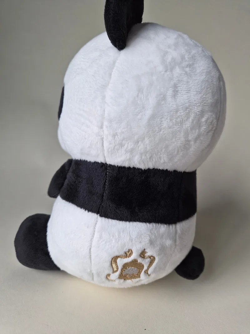 Rear view of the panda plush showing dense unfaded white plush and a small gold embroidered emblem low on the back