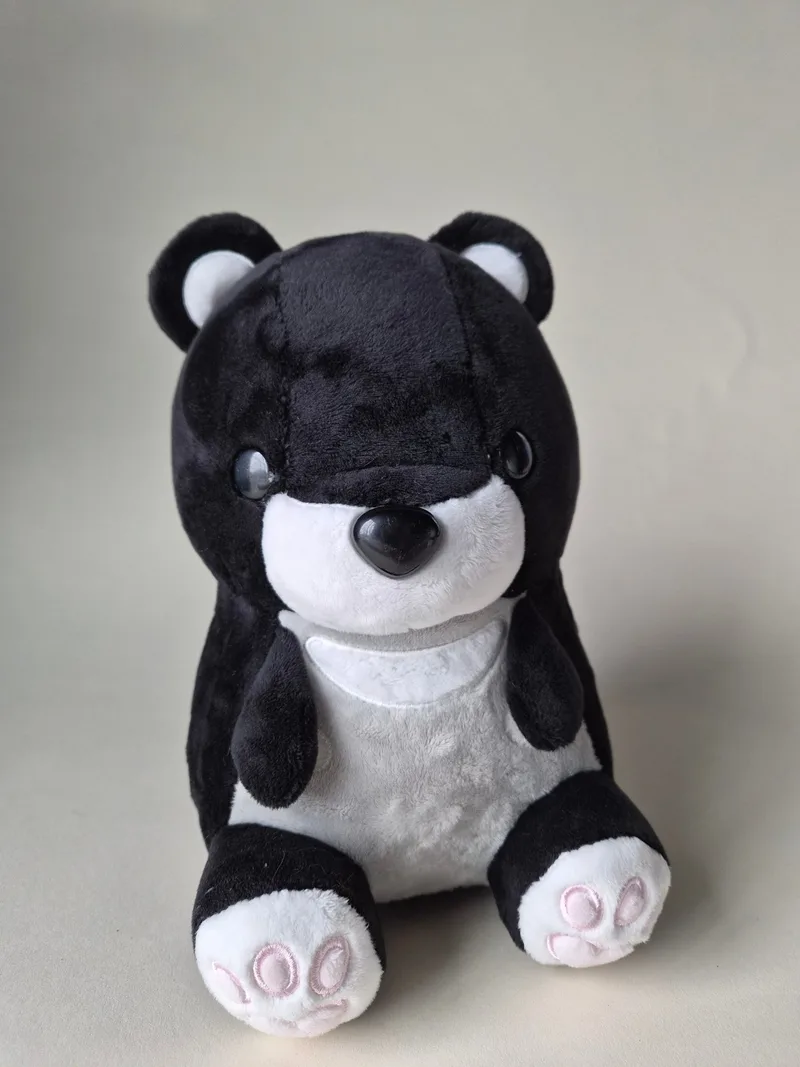 Black and white Bellzi teddy bear seated facing forward, arms out, with white muzzle and chest and pink toe pads on black soles