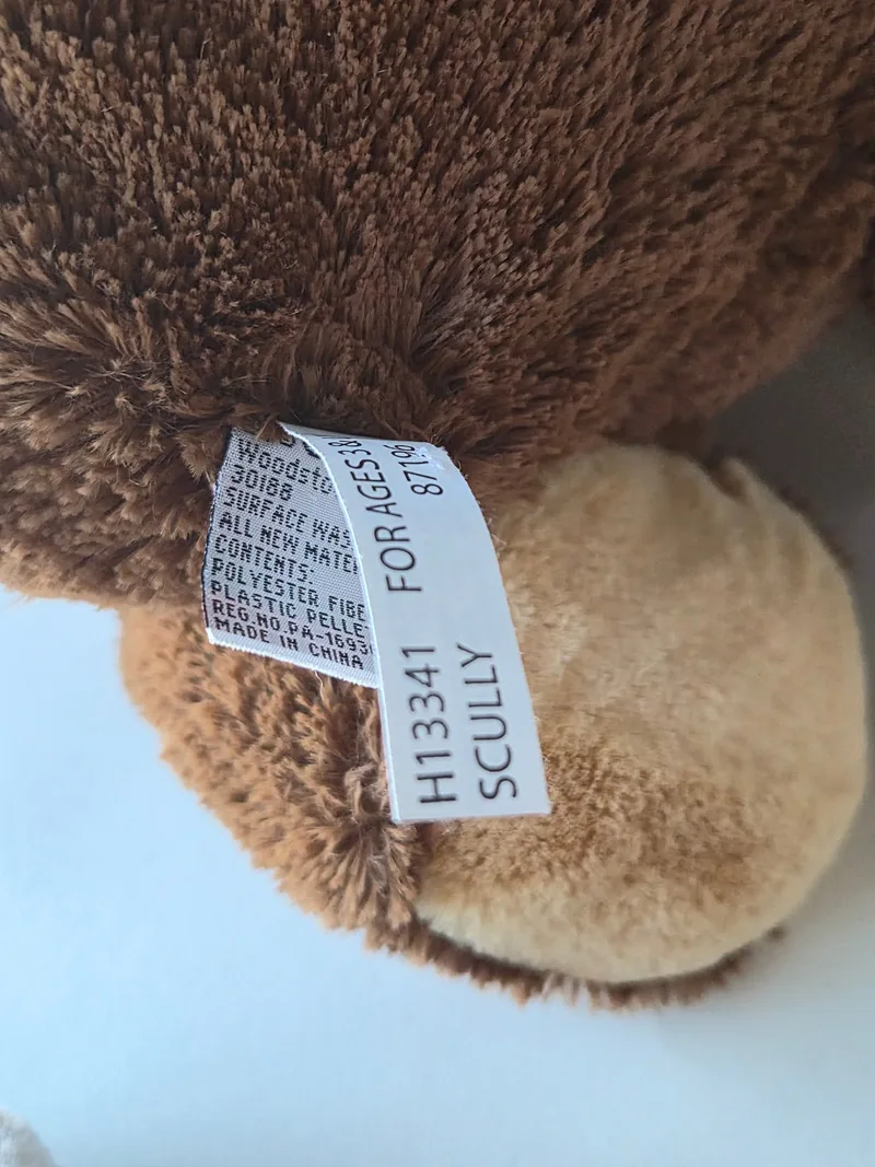 Close-up of the bear's fabric label reading SCULLY, style H13341, made in China