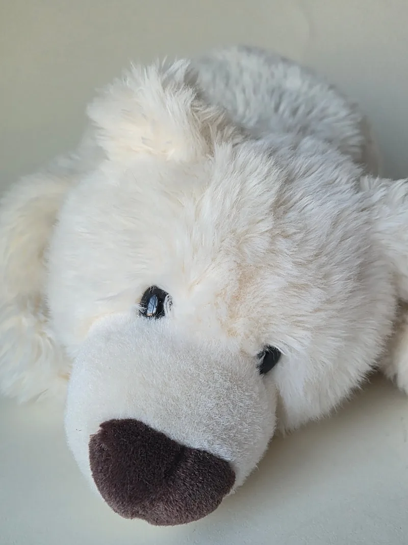 Close view of a cream-white plush polar bear's face, lying down, with small black eyes and a dark brown velour nose