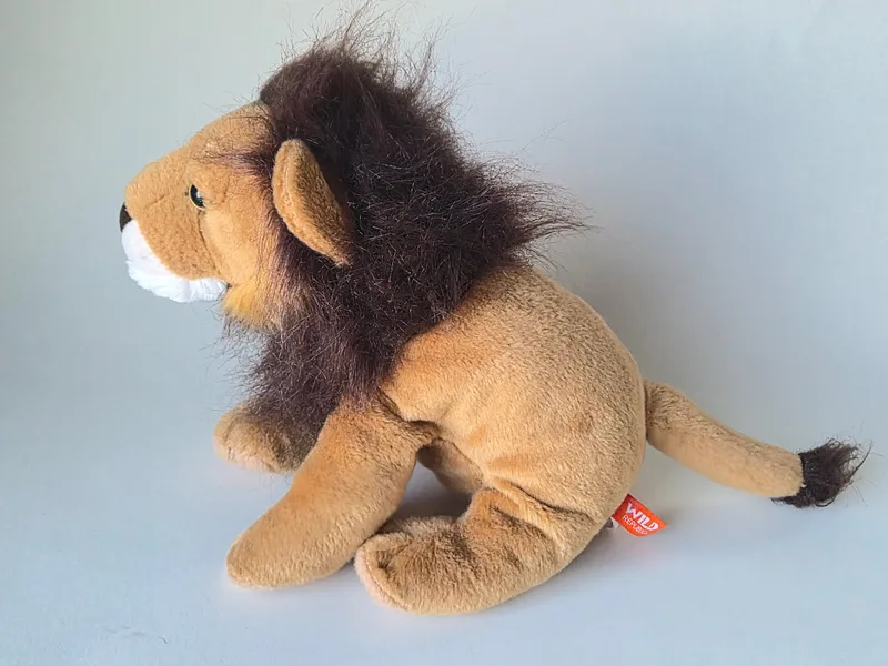 Side profile of the plush lion showing its full mane, lean body and tufted tail with an orange hip tag