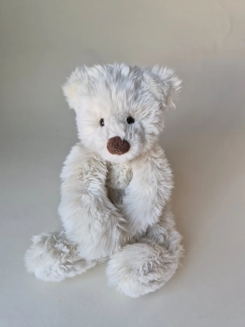 Cream long-pile teddy bear seated upright, front view, with small black eyes, a brown stitched nose, and broad shaggy feet