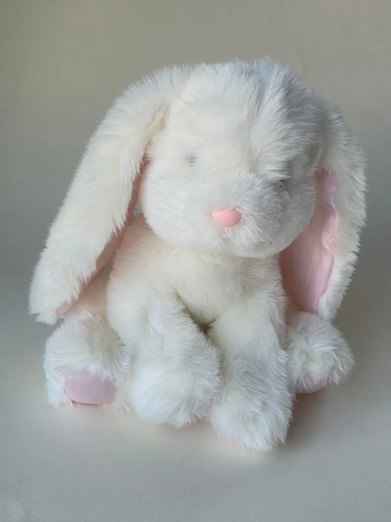 Small cream lop-eared plush bunny sitting upright, long ears lined in pale pink satin, stitched pink nose and close-set dark eyes