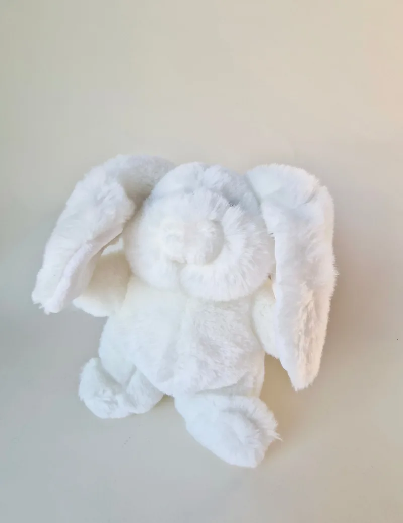 White long-eared plush bunny lying belly-down, seen from above, both ears flopped out to the sides