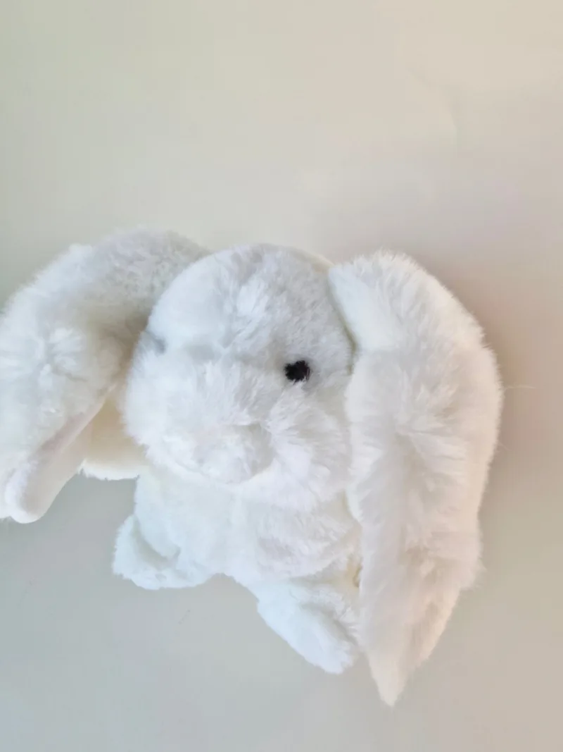 Close view of the bunny's face showing small black eye, stitched muzzle and dense white fur, one ear folded forward
