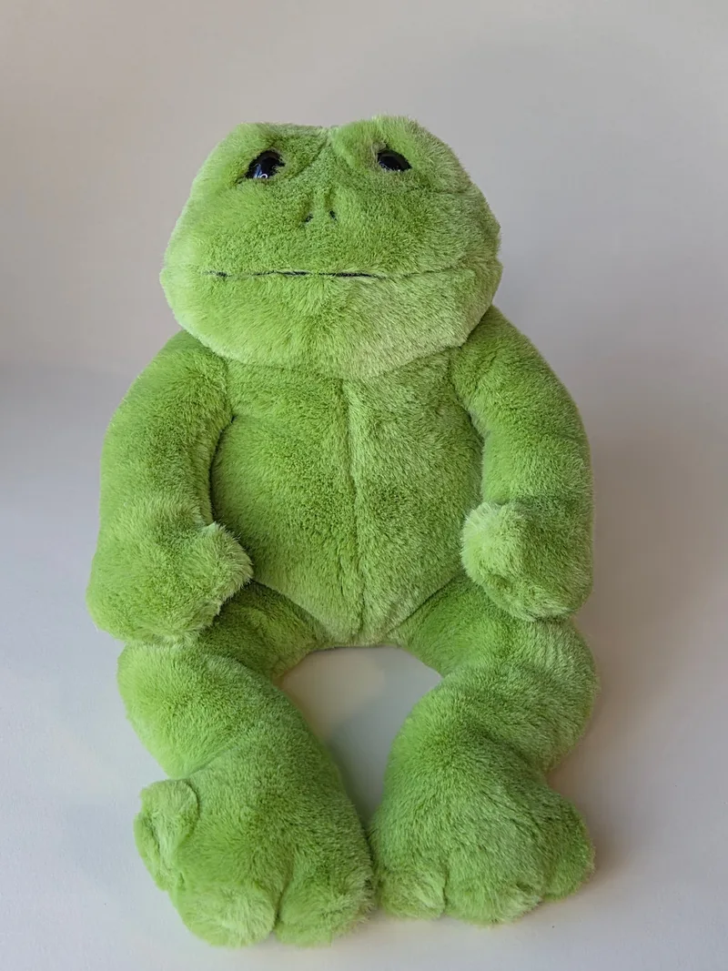 Large green plush frog sitting upright with legs extended forward, dark bead eyes and a long stitched mouth