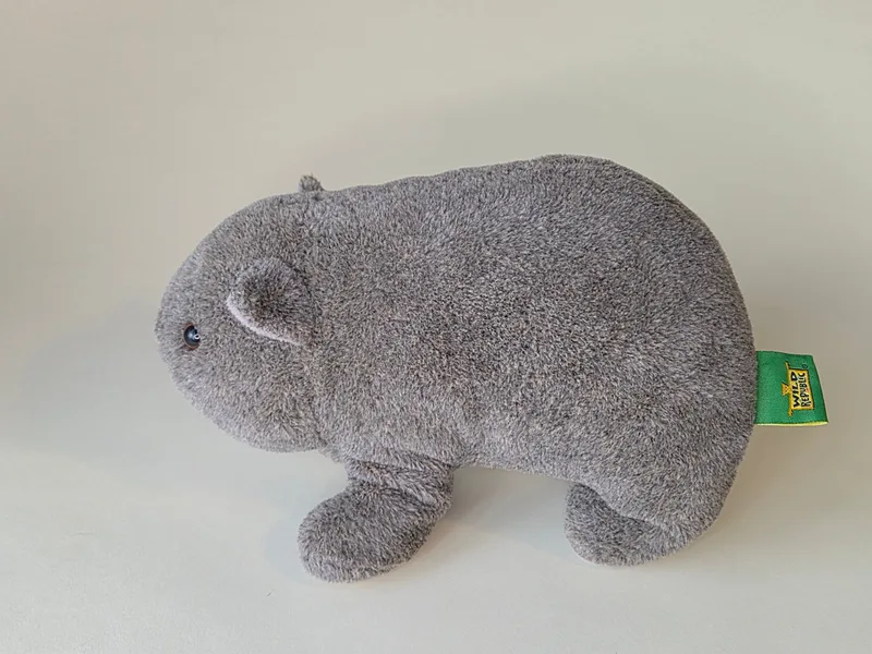Side profile of grey plush wombat showing green woven tag on the flank