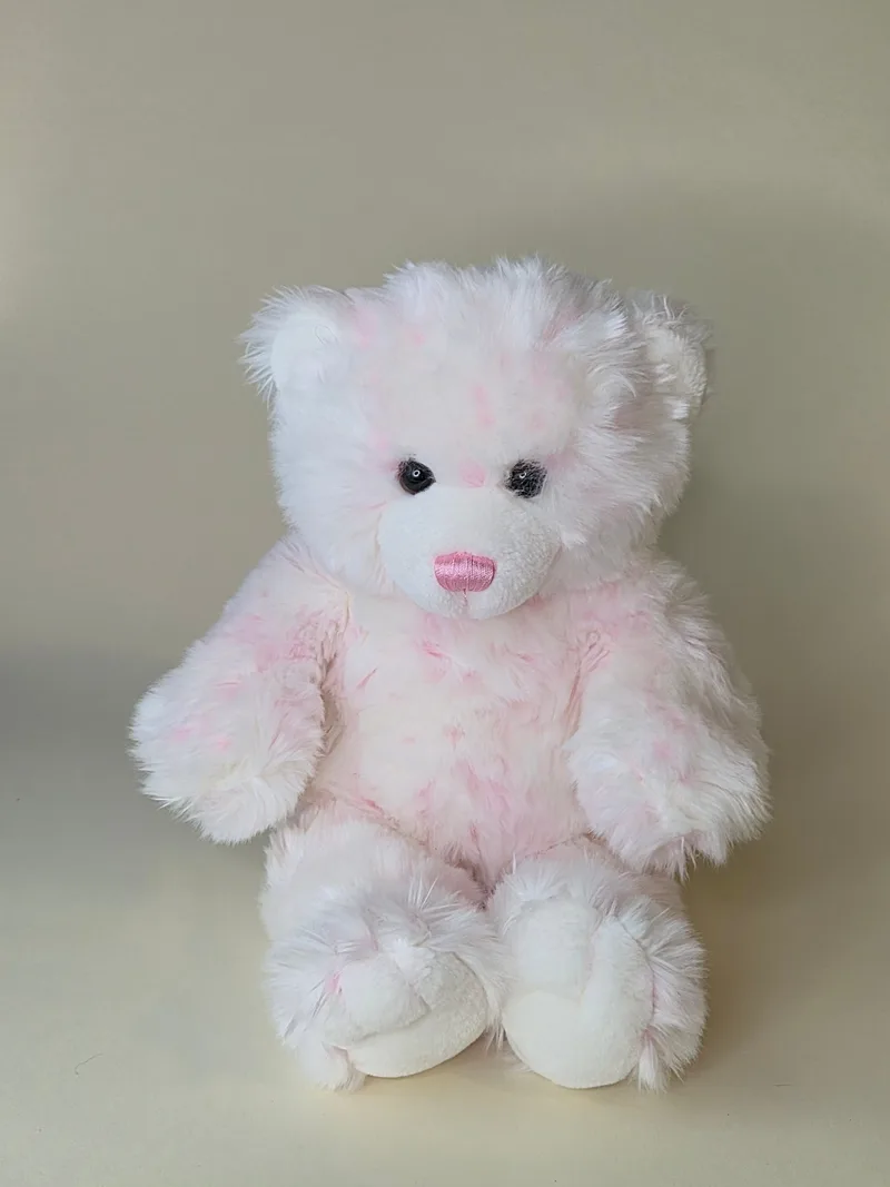 A seated white teddy bear with soft ballet-pink mottled fur, a pink satin nose, and black bead eyes.