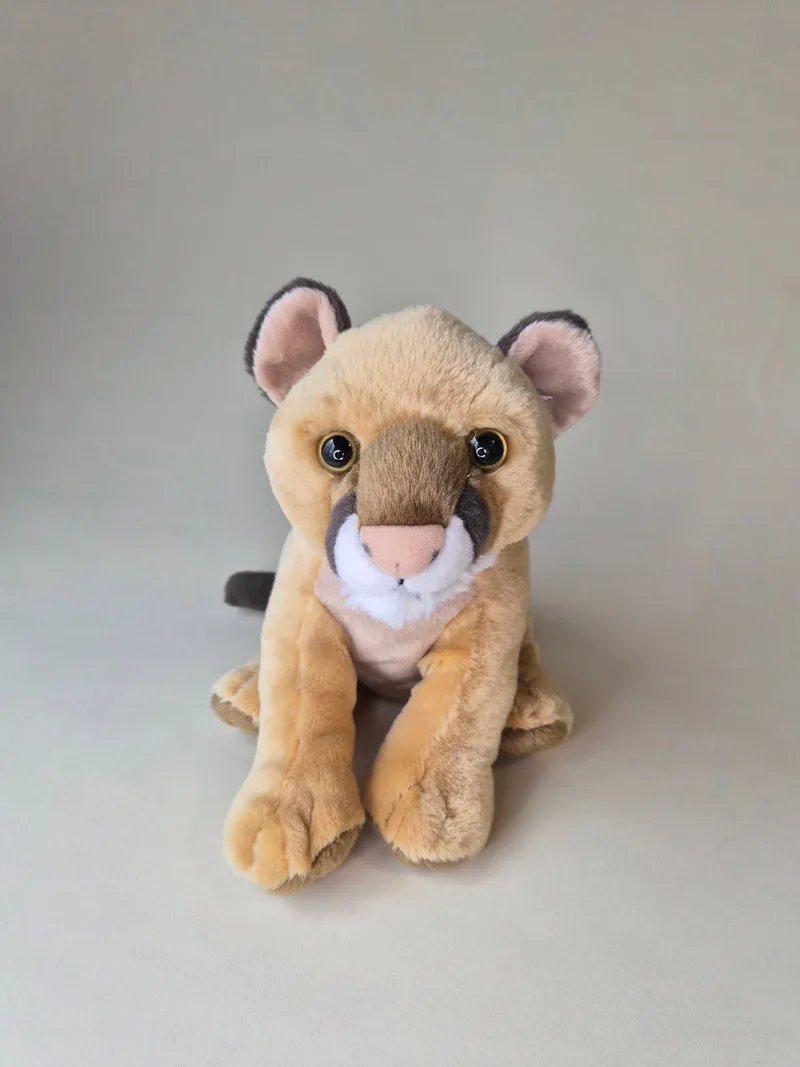 Front view of a seated tan lion cub plush with amber glass eyes, pink nose, and white chest fur.