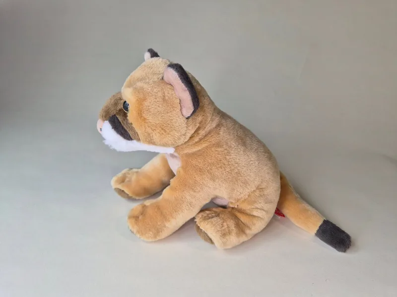 Side profile of the lion cub plush showing brown-tipped ears, black-tipped tail, and tan paws.