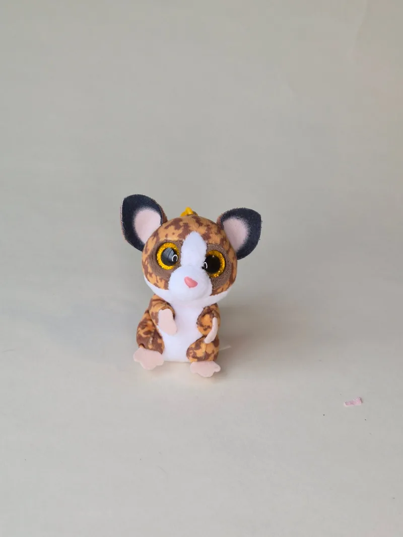 Small leopard-print keychain plush with large sparkly gold eyes, pink nose, and a yellow plastic clip, standing against a plain background.