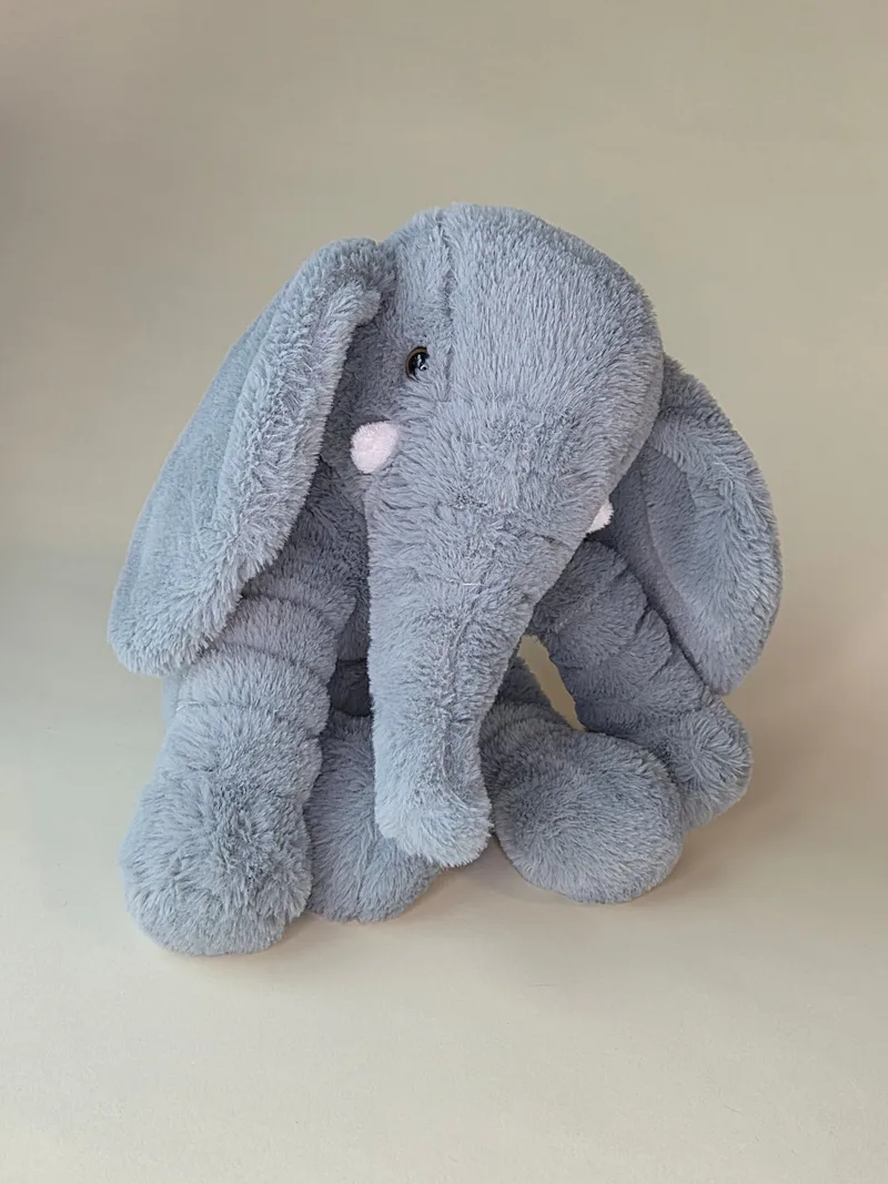 Grey plush elephant sitting upright with large floppy ears and pink cheek patches, front view