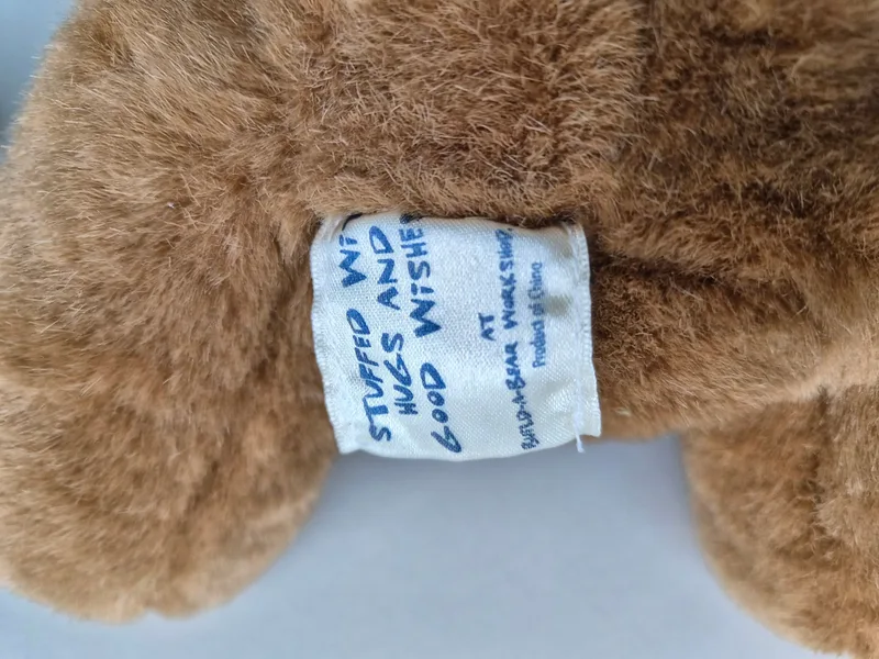 Close-up of the fabric tag sewn into the bear's back seam, reading a Build-A-Bear Workshop label.