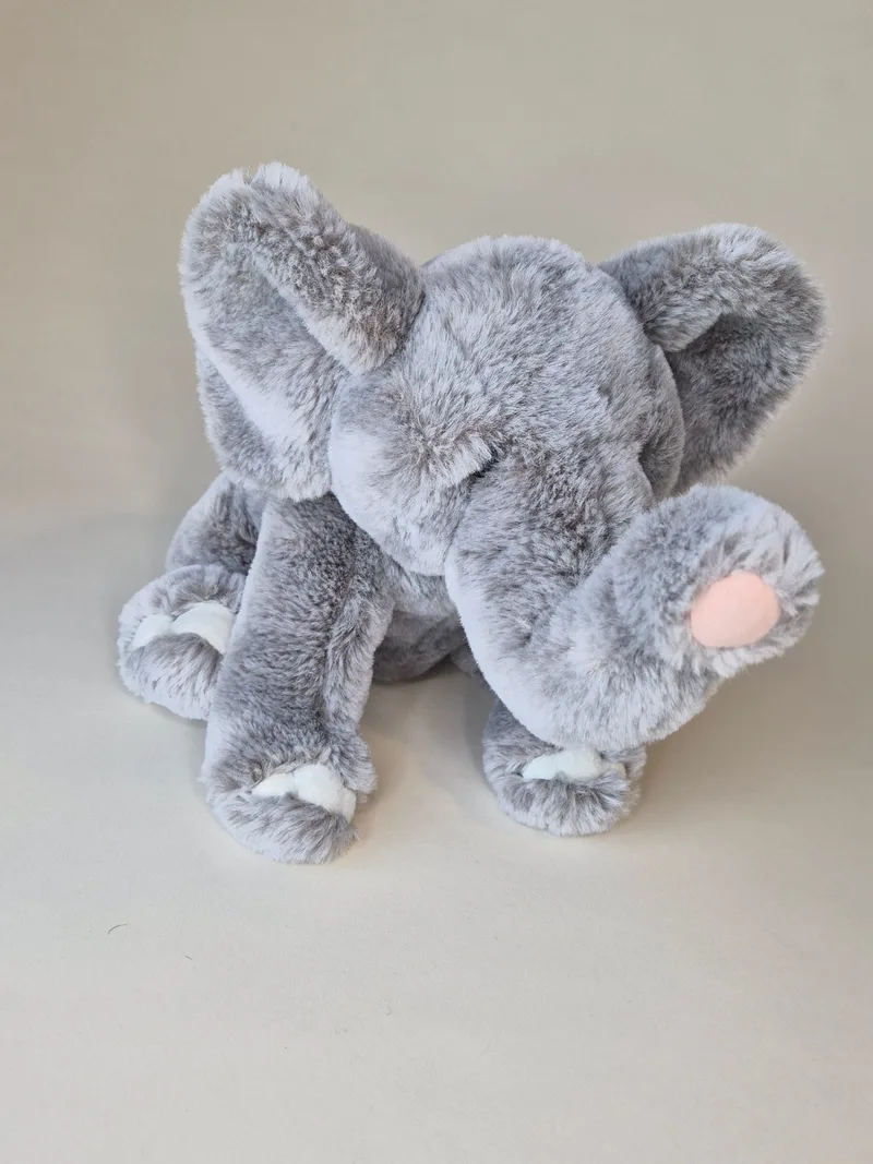 Grey plush elephant lying down with trunk curled toward blush-pink tip and ears folded forward
