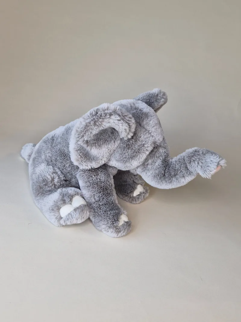 Side view of grey plush elephant showing floppy ears, curled trunk, and small tufted tail