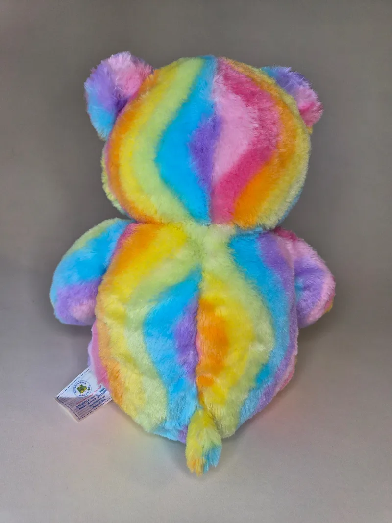 Back view of the rainbow teddy bear showing matching stripe pattern and a small fabric tag at the lower seam