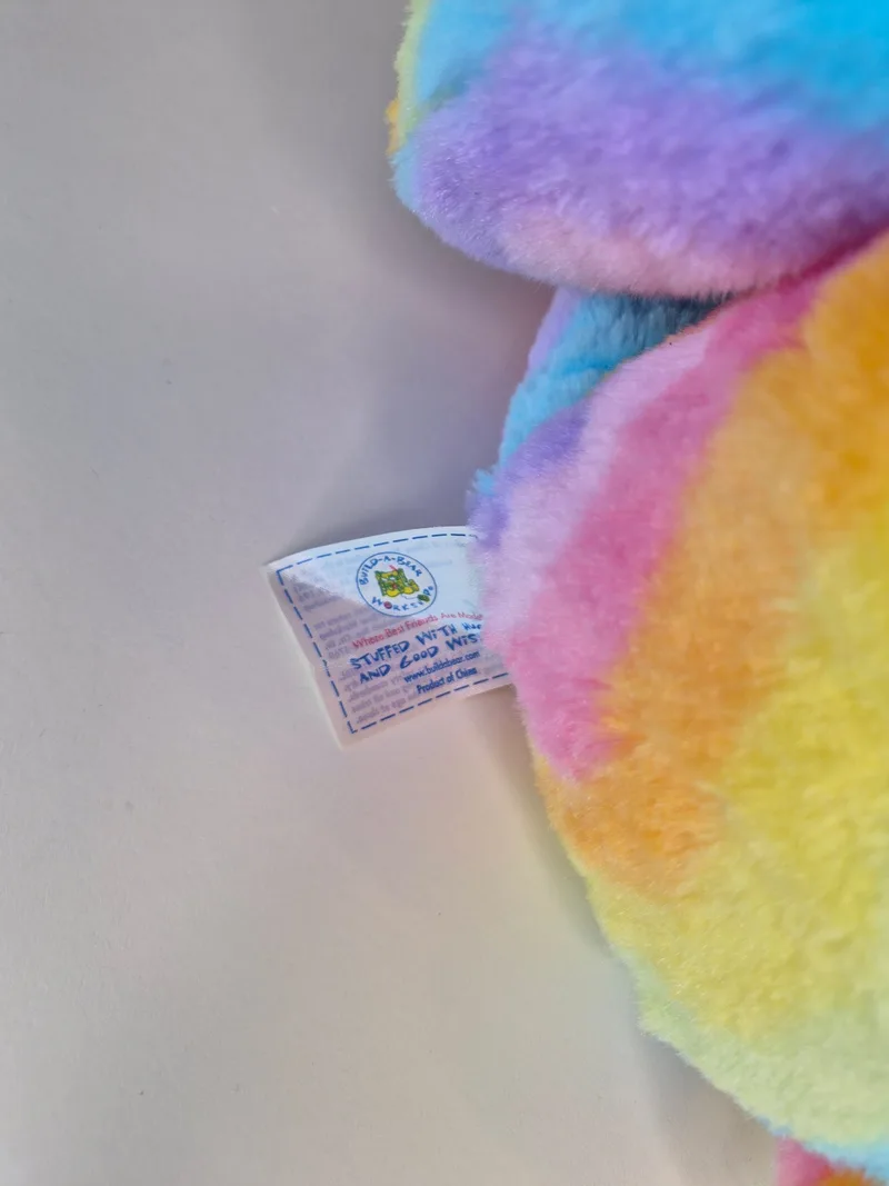 Close-up of the stitched Build-A-Bear Workshop tag reading 'stuffed with love and good wishes' against the bear's colorful fur